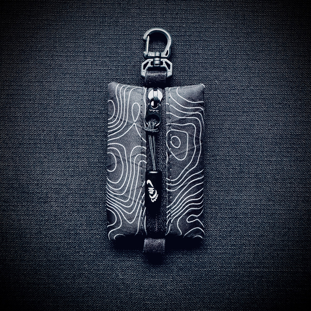 Black topo X-Pac micro utility pouch with black YKK zip, engraved Tread Lite aluminium pull and swivel carabiner hook.