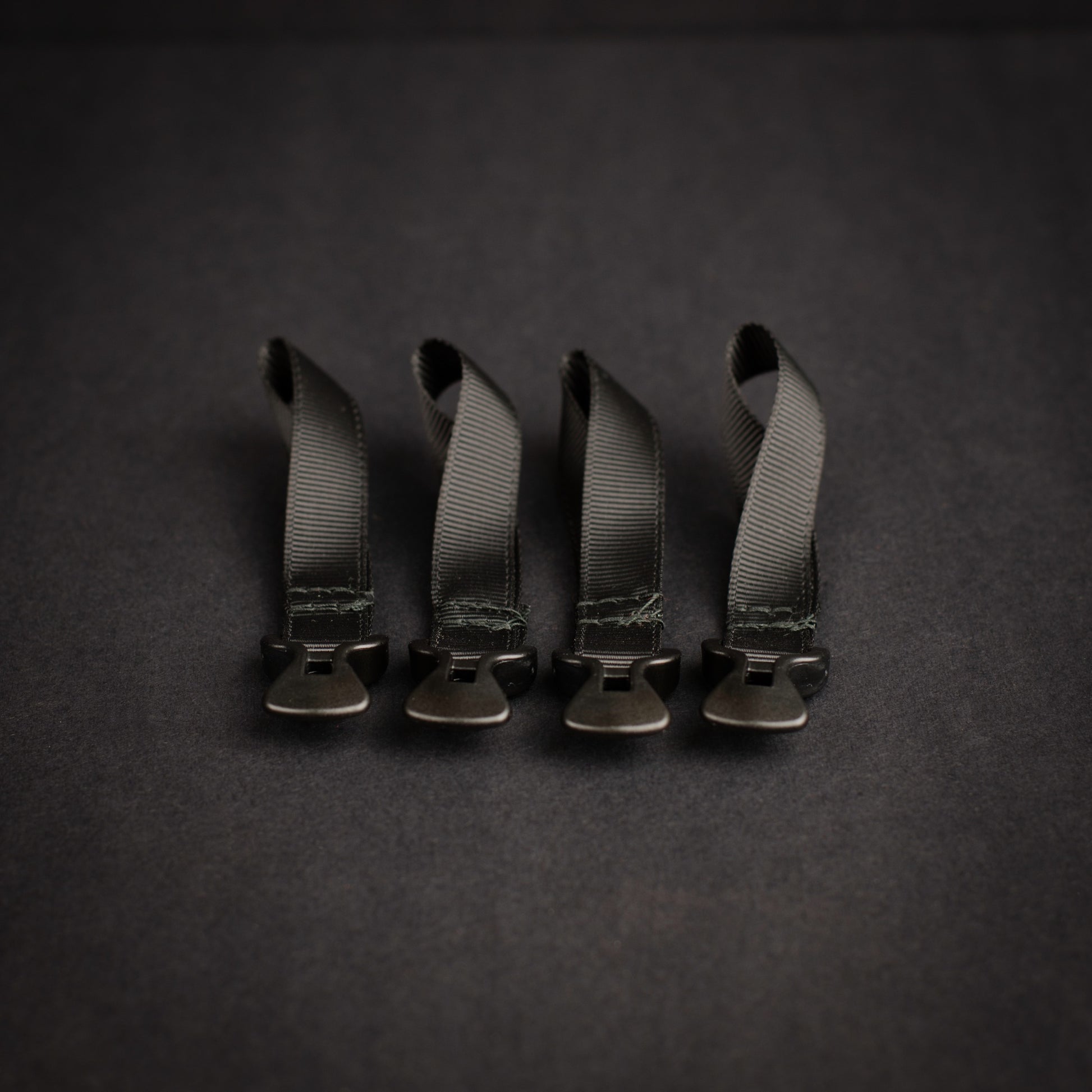 Four black LineLoc 3 self-tensioning tarp adjusters pre-fitted to black grosgrain loops for ultralight shelter and guyline systems.