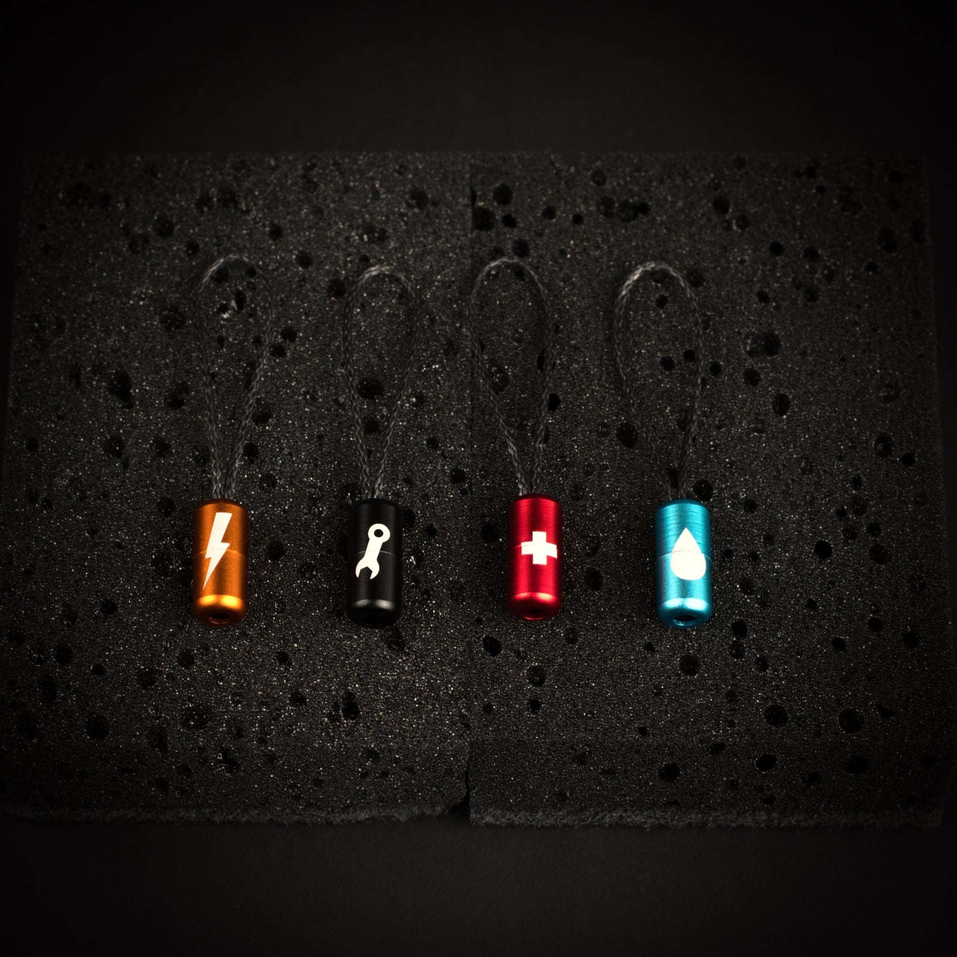 Four ultralight engraved aluminium gear identifier zipper pulls with Dyneema cord loops for power, keys, first aid and water.