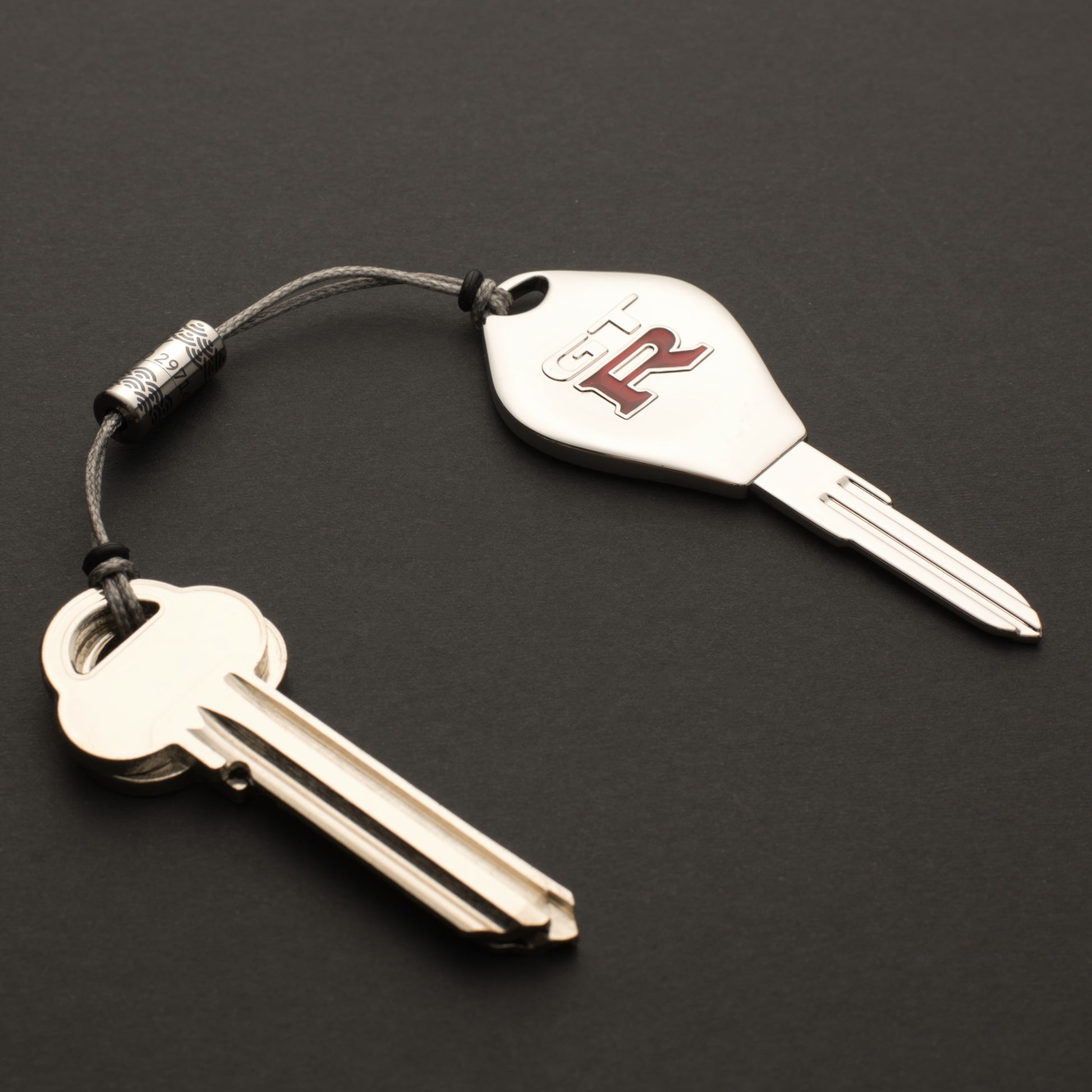 Personalised titanium Bow-Ti separable key link connecting two keys with Dyneema cord and engraved titanium body