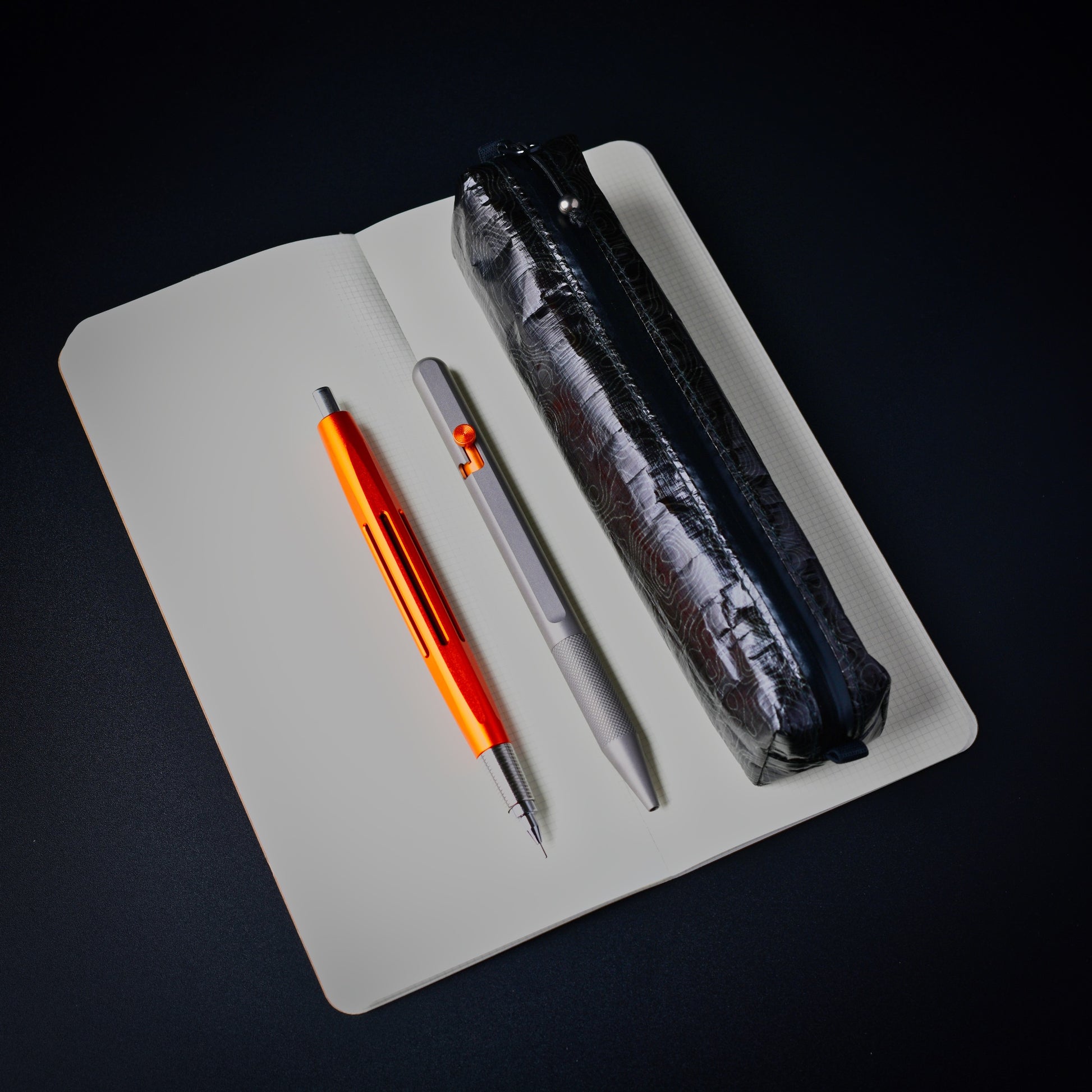 Dyneema Topo Writing Instrument Case alongside a notebook and pens for size reference.