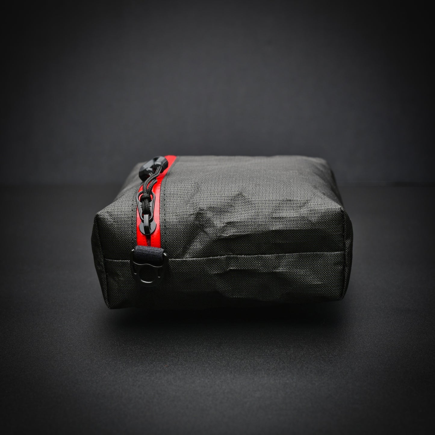 End view of a black EcoPak Ultra™ gusseted zip pouch with red YKK® AquaGuard® zip, glove-compatible zip pull and side D-ring.