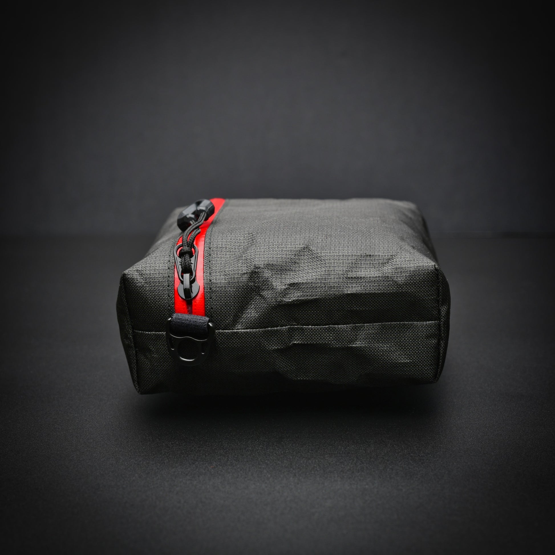 End view of a black EcoPak Ultra™ gusseted zip pouch with red YKK® AquaGuard® zip, glove-compatible zip pull and side D-ring.