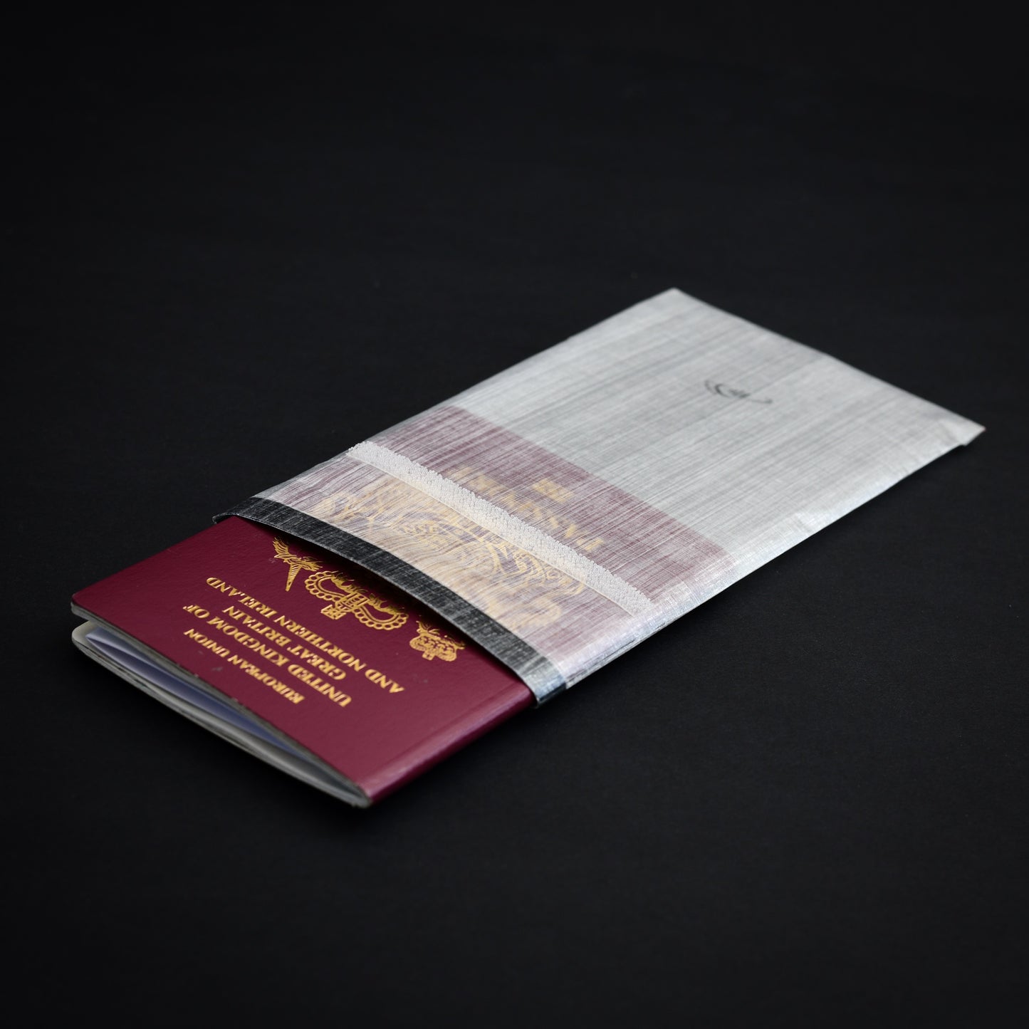 Handmade bonded Dyneema Composite Fabric roll-top passport sleeve with UK passport partially inserted, showing the lightweight, highly water-resistant travel wallet design.