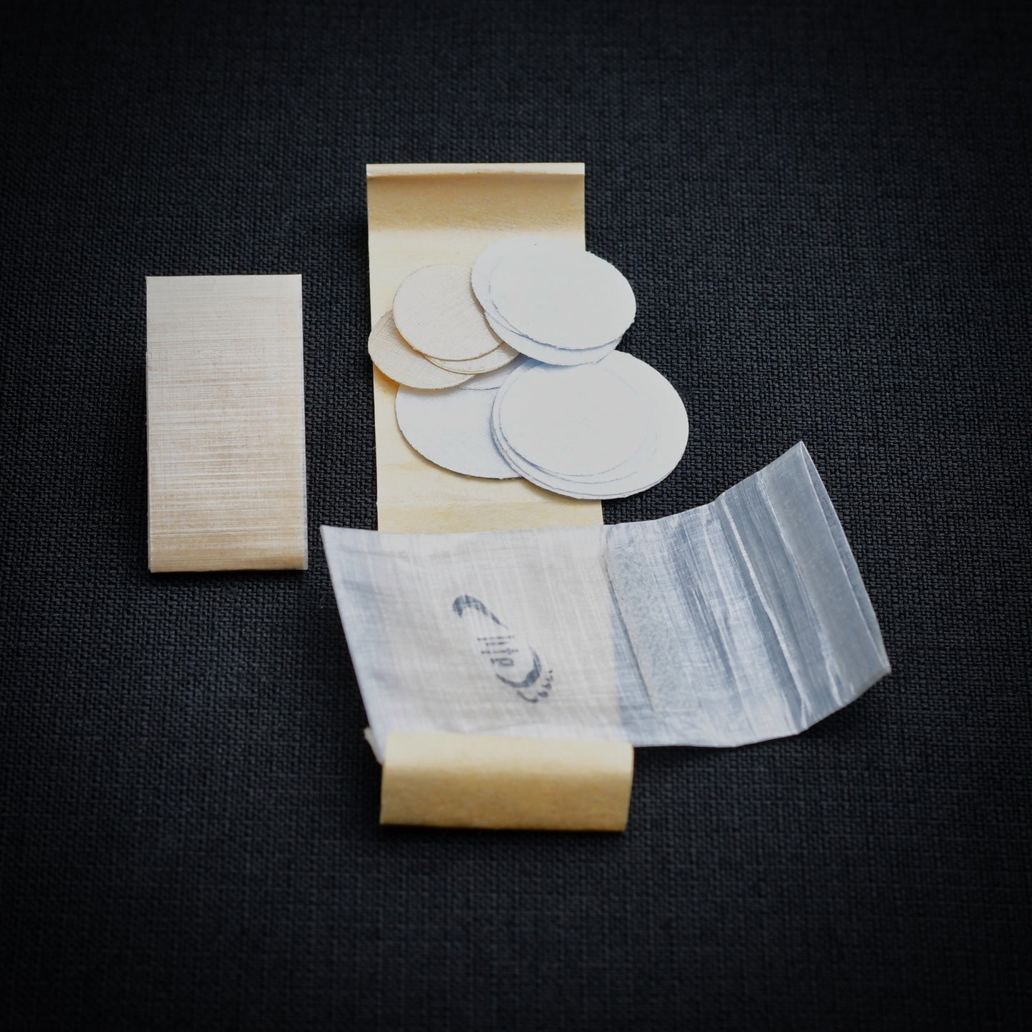 DCF repair kit contents showing circular self-adhesive patches in three sizes, 15 cm repair strip, kraft release liners and mini roll-top dry bag.