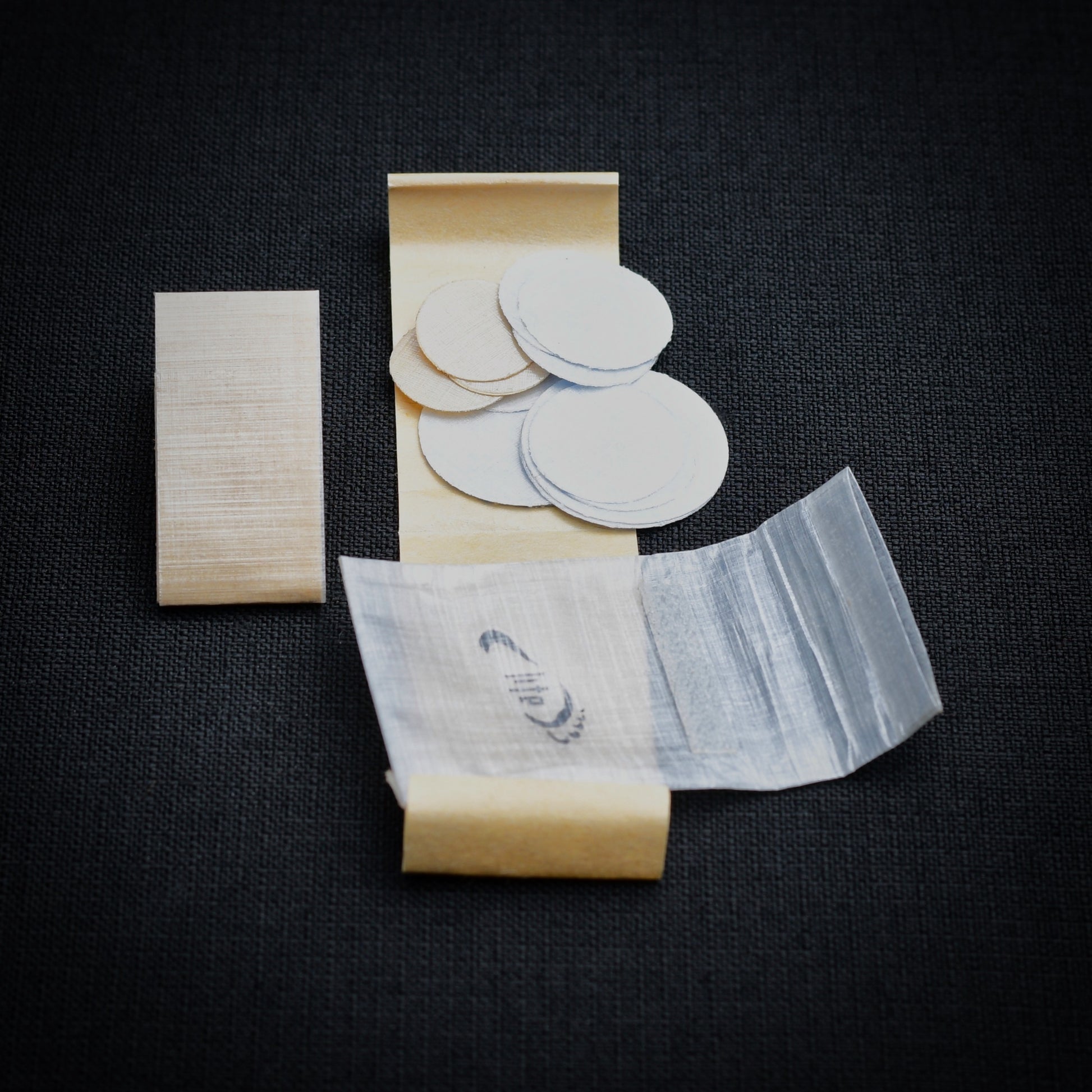 DCF repair kit contents showing circular self-adhesive patches in three sizes, 15 cm repair strip, kraft release liners and mini roll-top dry bag.