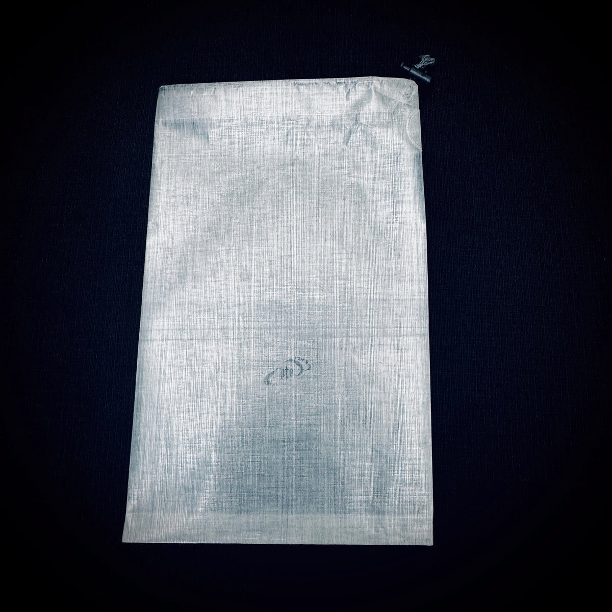 Empty white bonded DCF stuff sack laid flat on a black background