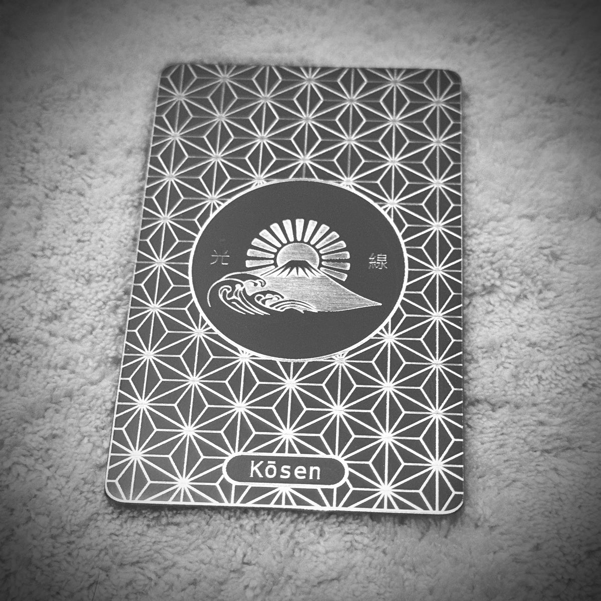Portrait view of Kōsen Object 001 Inner Strength titanium art card with Asanoha pattern, Mount Fuji, breaking waves and rising sun.