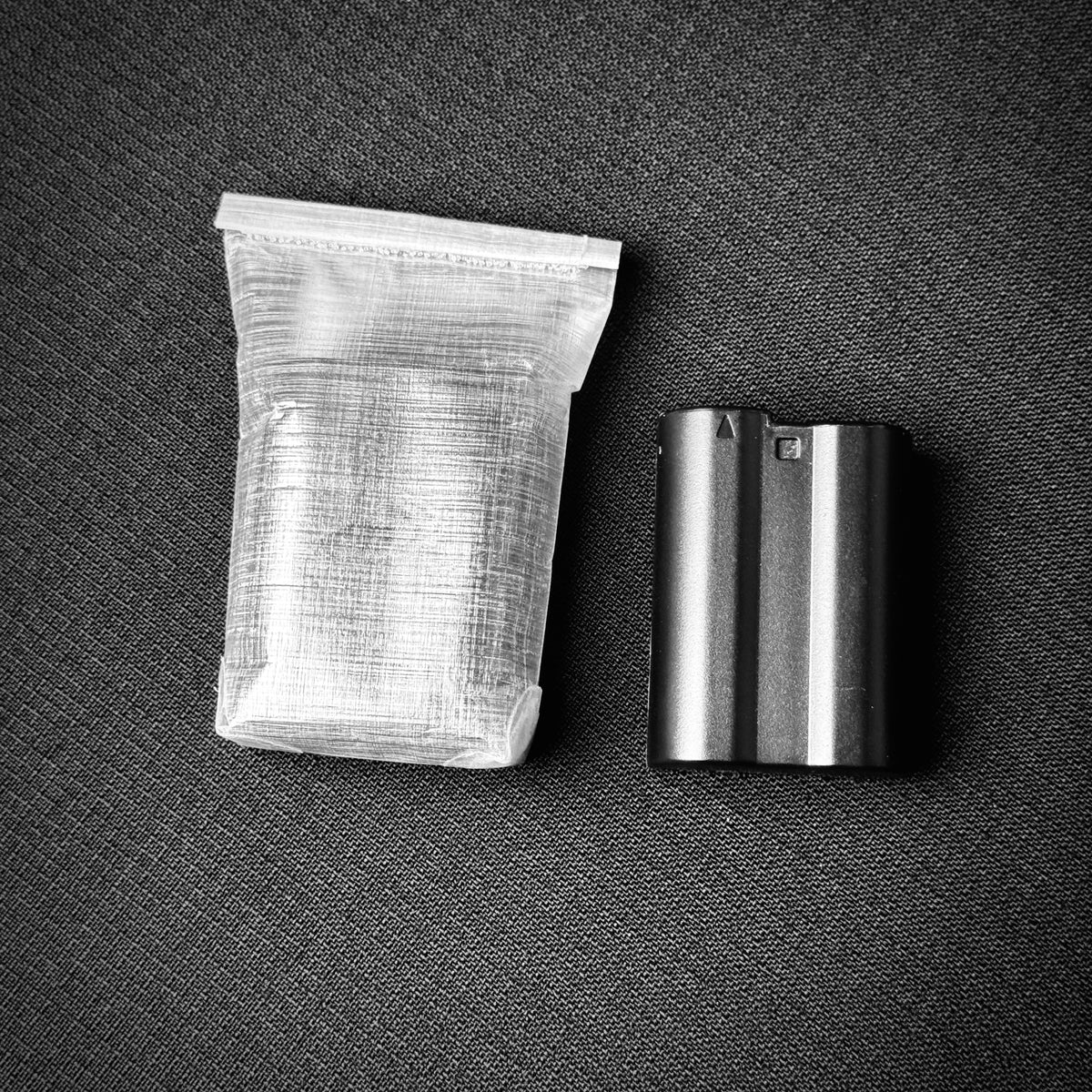 DCF battery dry bag beside a camera battery for size comparison.