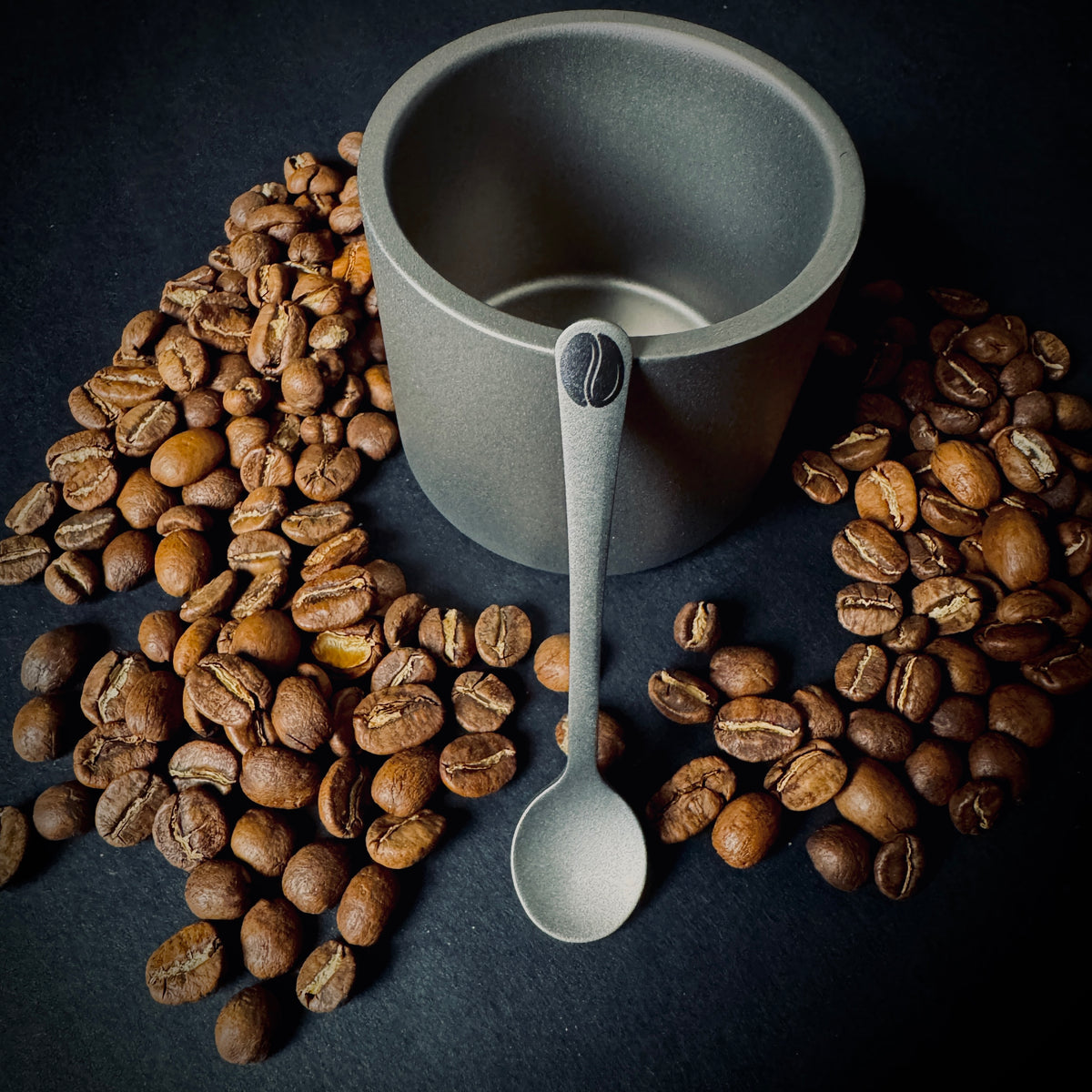 Grade 5 titanium coffee spoon with laser marked coffee bean design, displayed with coffee beans and a titanium cup.