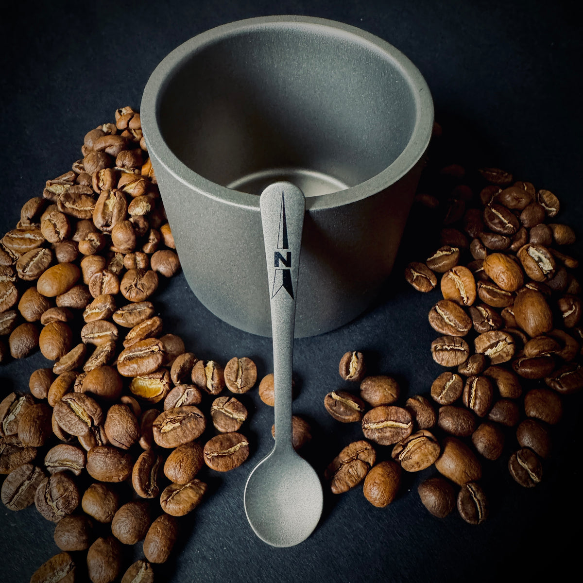 Grade 5 titanium coffee spoon with North navigation design, displayed with coffee beans and a titanium cup.